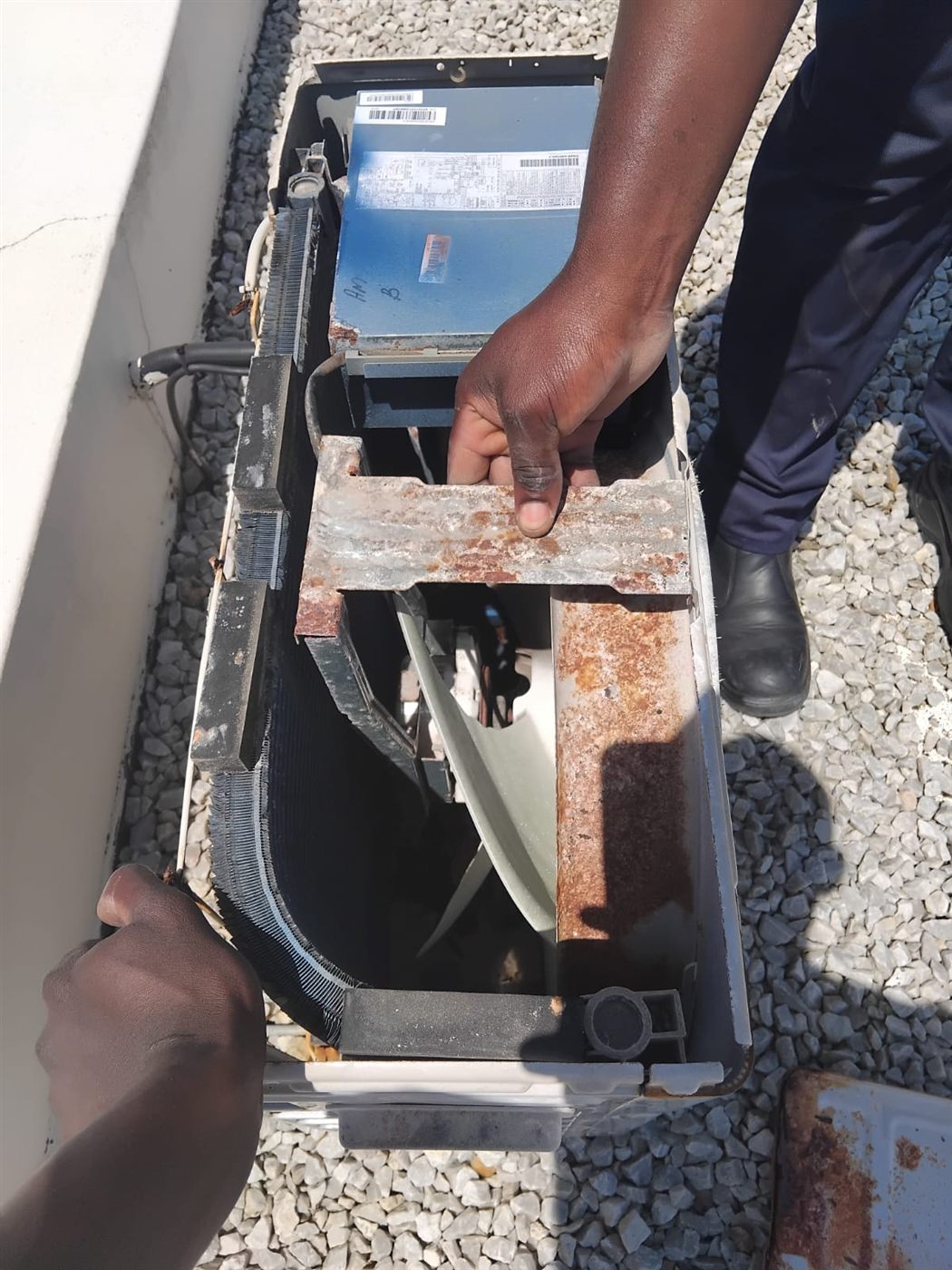 Technician inspecting rust on the internal frame of an aircon outdoor unit